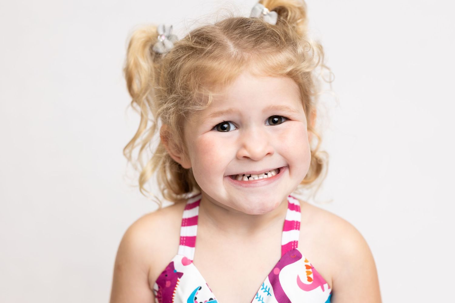 Studio portrait of a cheerful child in a striped swimsuit with blonde pigtails.