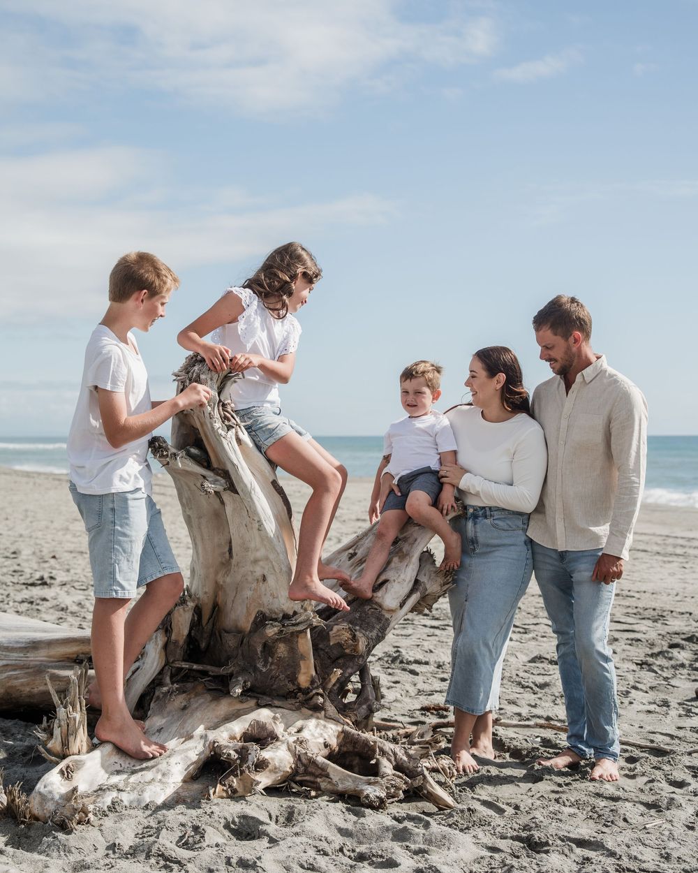 family gathered on a log on a beach near hokitika