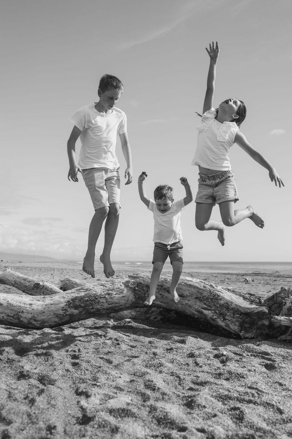 kids jumping together off a log on a beach
