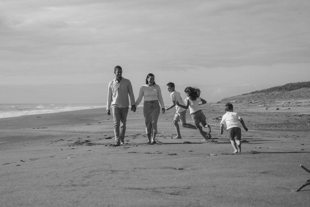 kids chasing each other around parents walking on the beach