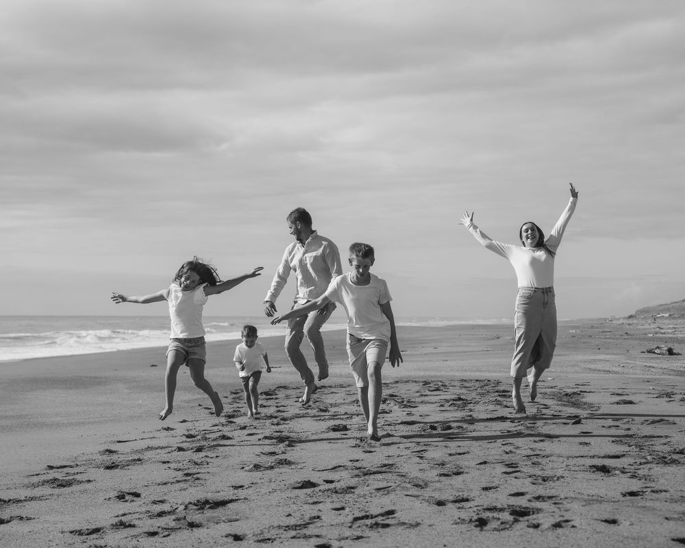 family running and jumping together on Mananui Beach south of Hokitika in black and white