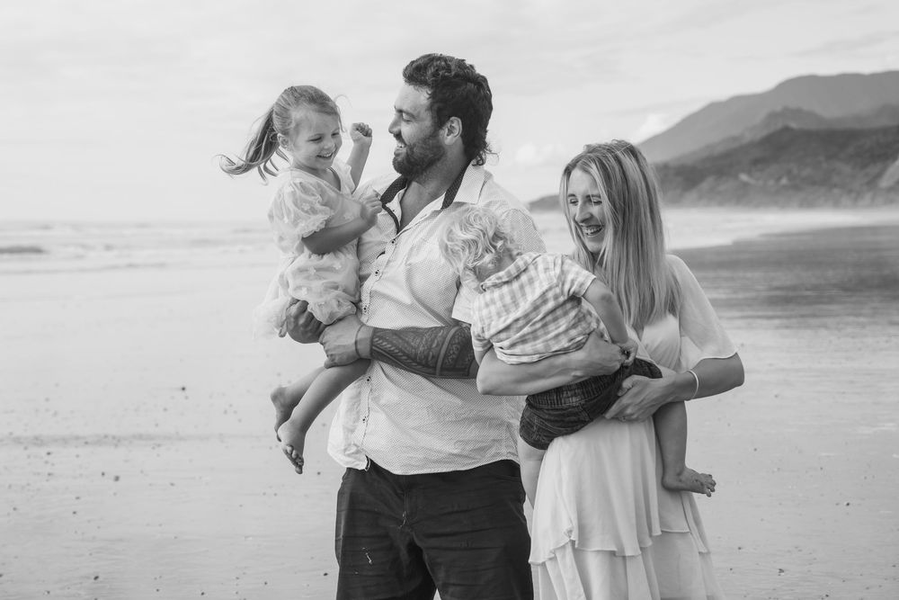 Family cuddling dancing and laughing together at Rapahoe beach north of Greymouth on the West Coast