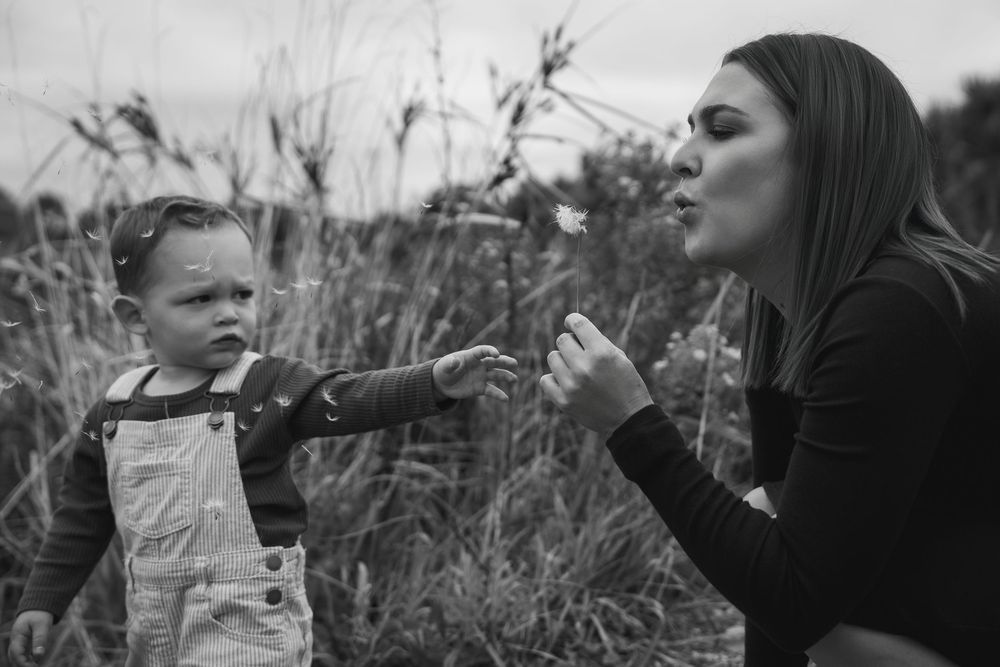 mother blowing dandelion wishes with toddler black and white