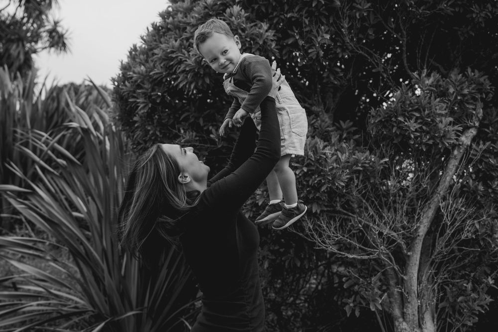 mother holding toddler son in the air, laughing in Greymouth