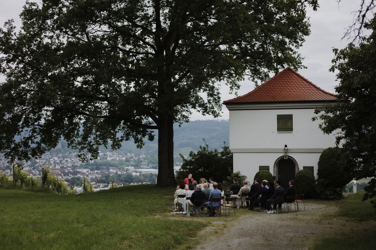Small white tower building on a hilltop with people gathered for an outdoor event.