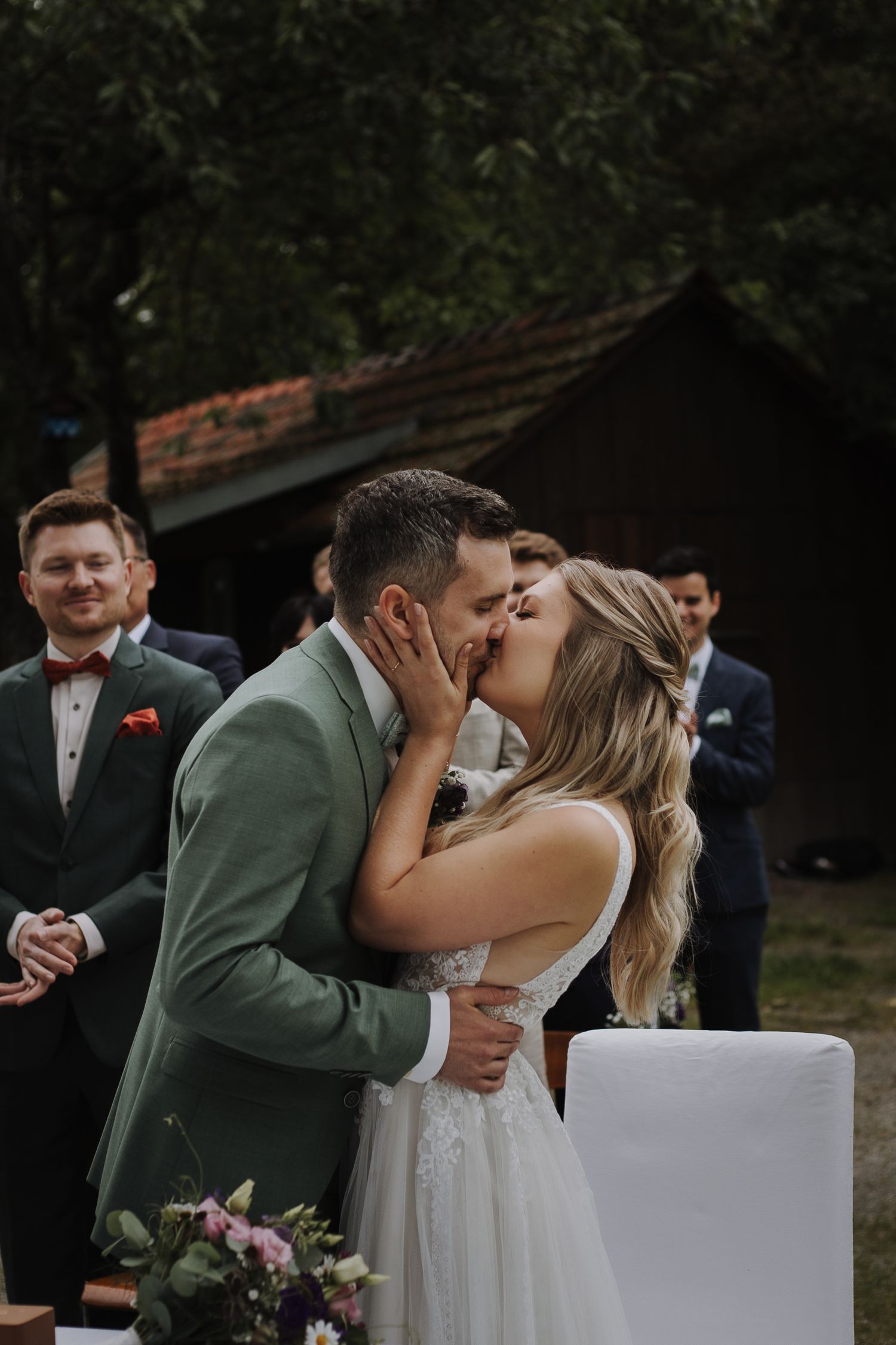 Bride and groom sharing passionate kiss during outdoor ceremony while guests look on.
