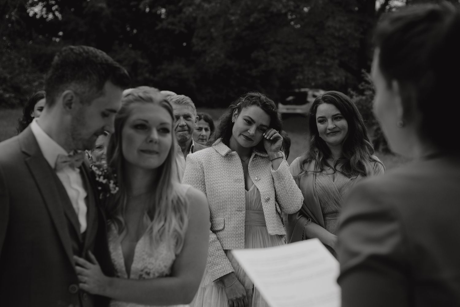 Black and white candid photo of wedding guests laughing during outdoor reception.