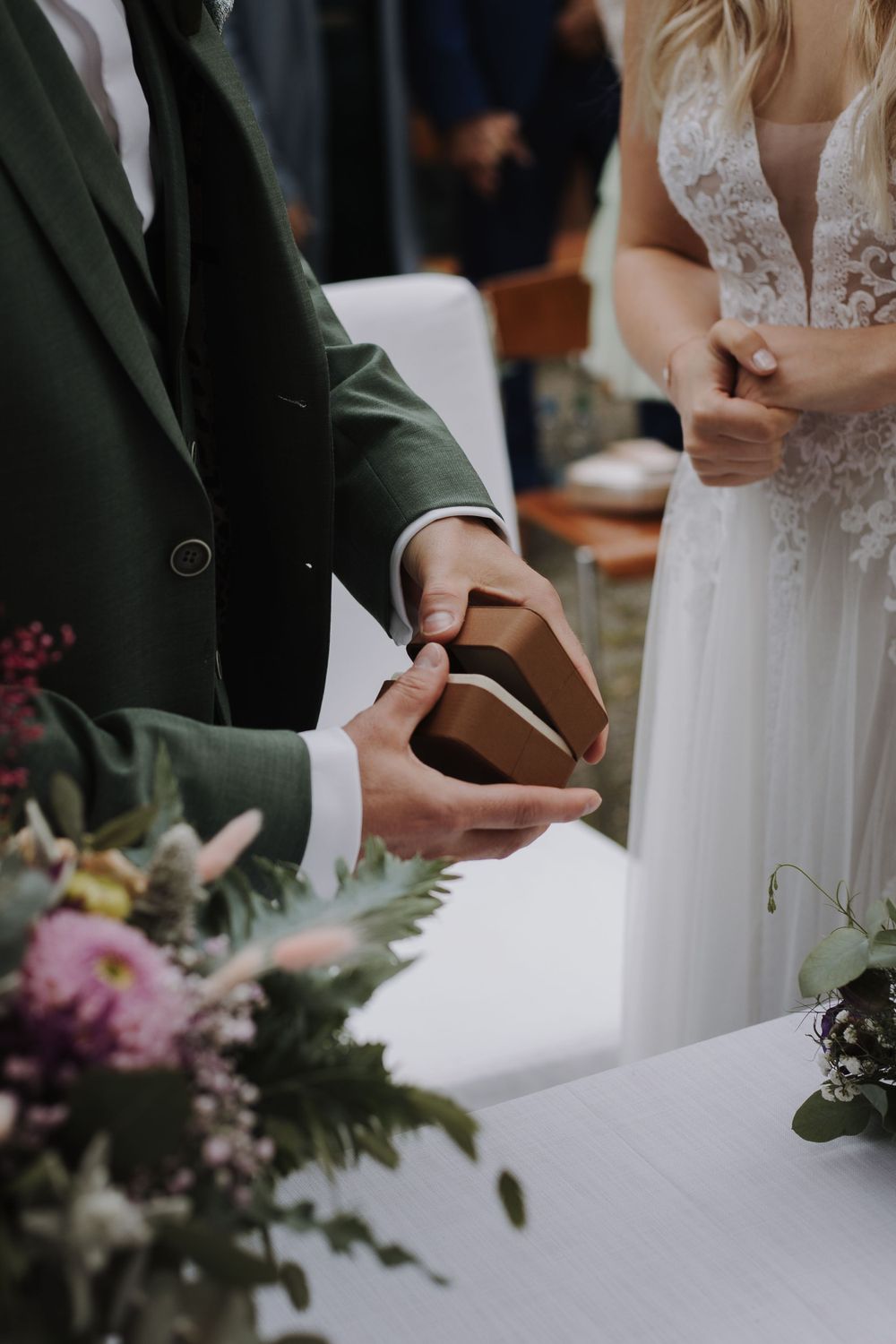 Close-up of couple's hands during wedding ceremony with floral decorations.