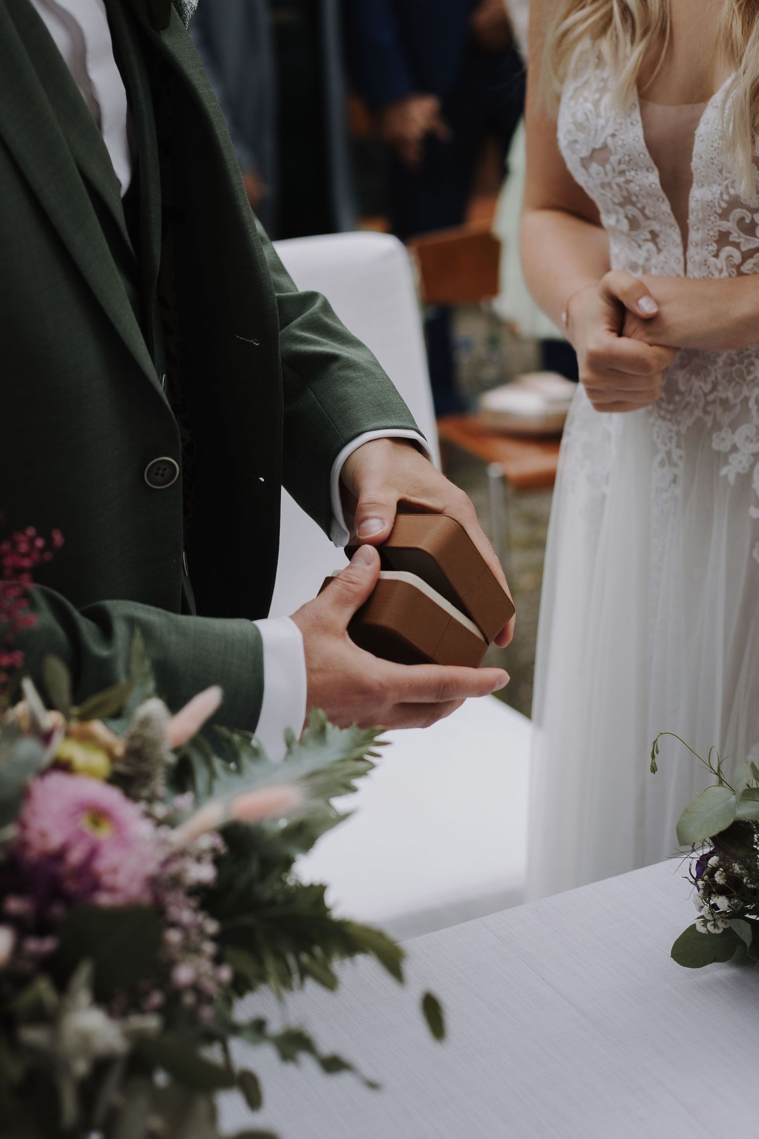 Close-up of couple's hands during wedding ceremony with floral decorations.