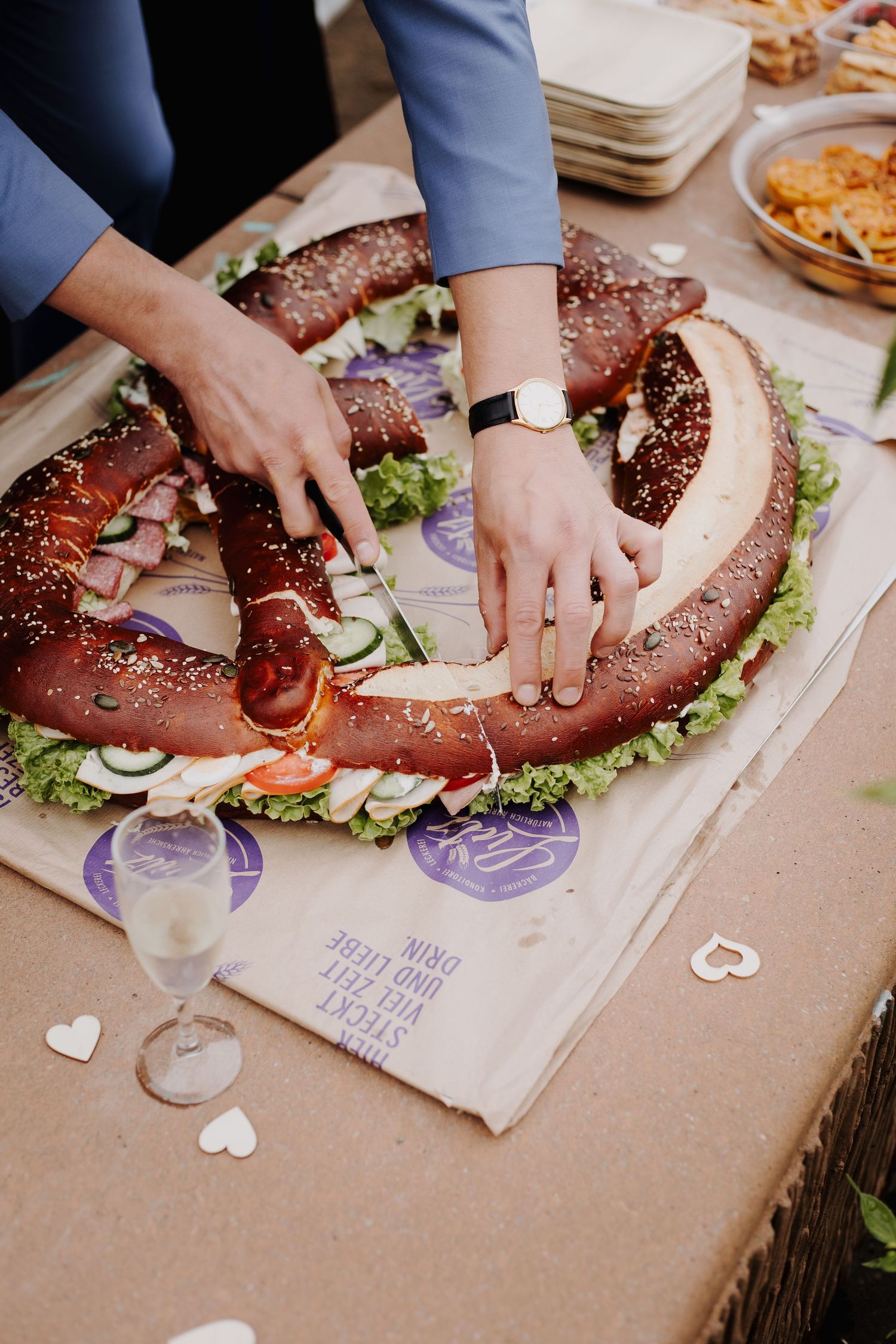 Hands arranging a creative charcuterie board in a pretzel shape on a rustic table.