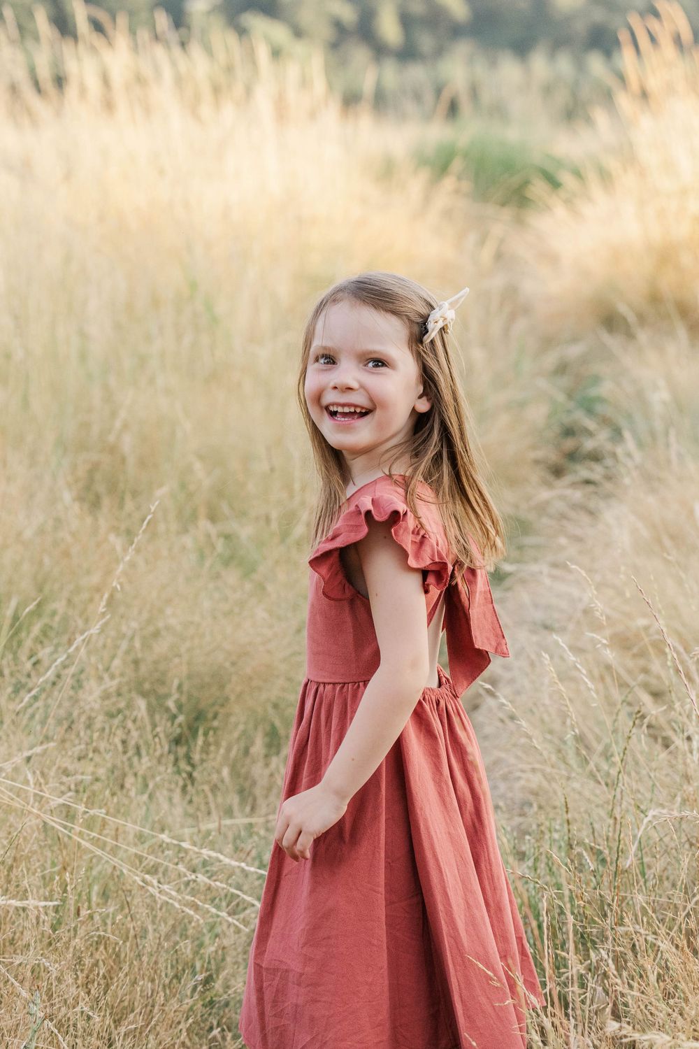 Cheerful young girl in a red dress smiling over her shoulder in a golden grass field.