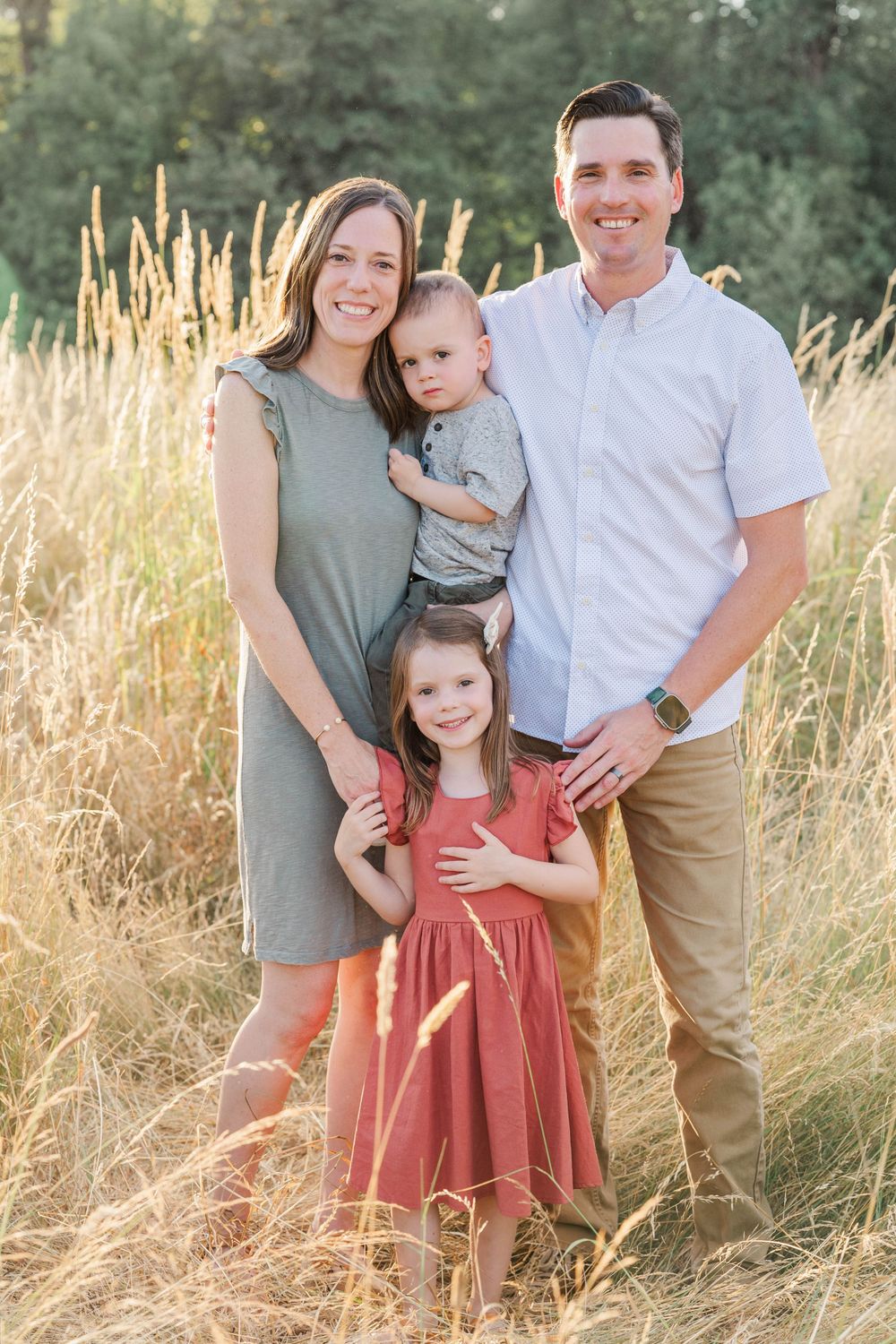 Happy family of four posing together in a sunlit golden grass field during fall season.