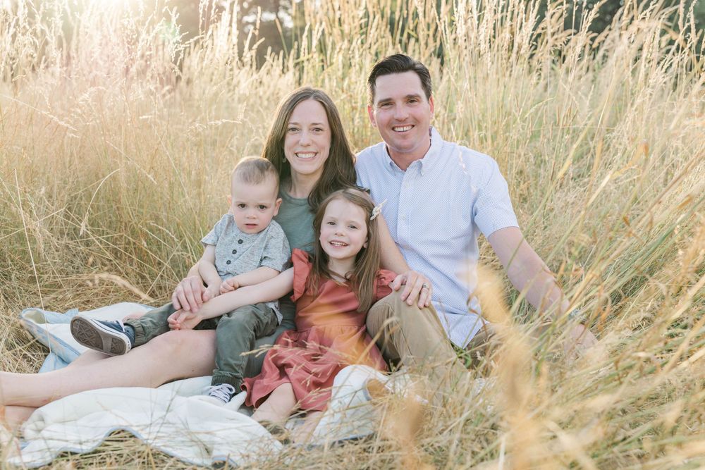 Happy family of four sitting together on a blanket in a golden sunlit field.