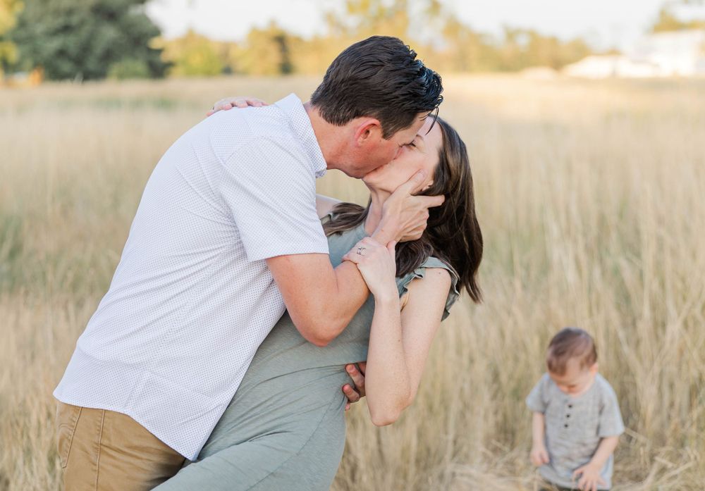 Couple sharing a romantic kiss in a golden wheat field during an outdoor family photo session.