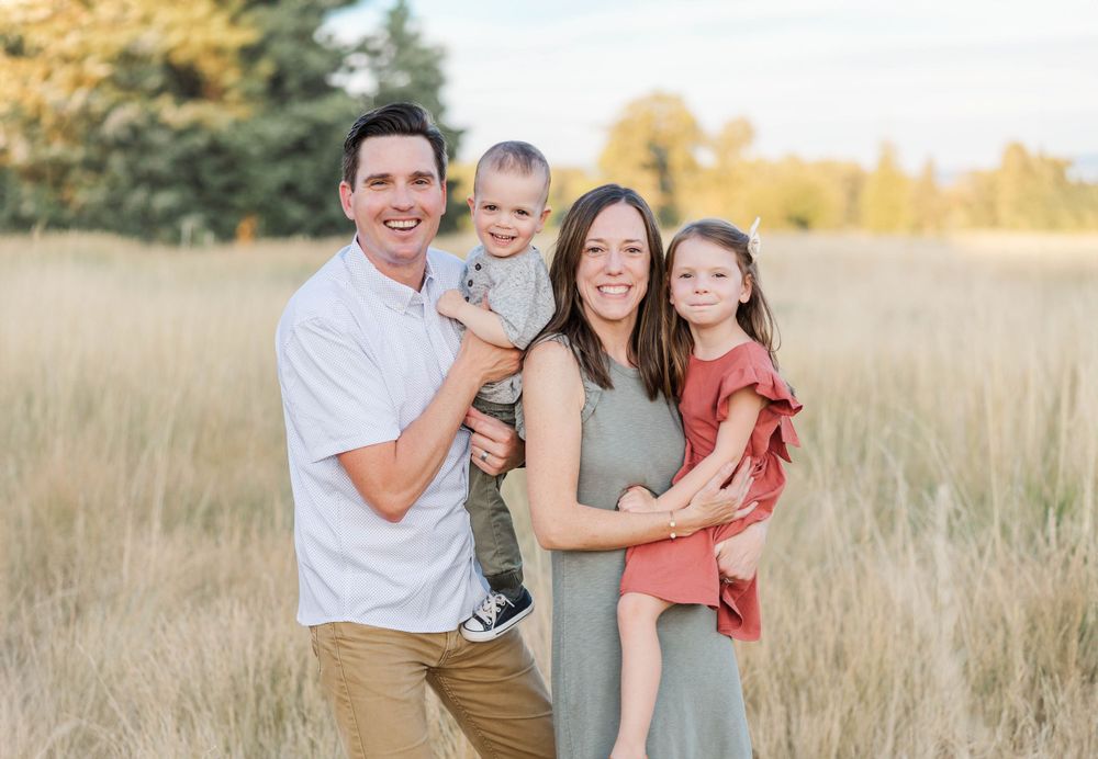 Happy family of four smiling together in a golden field during a sunny outdoor portrait session.