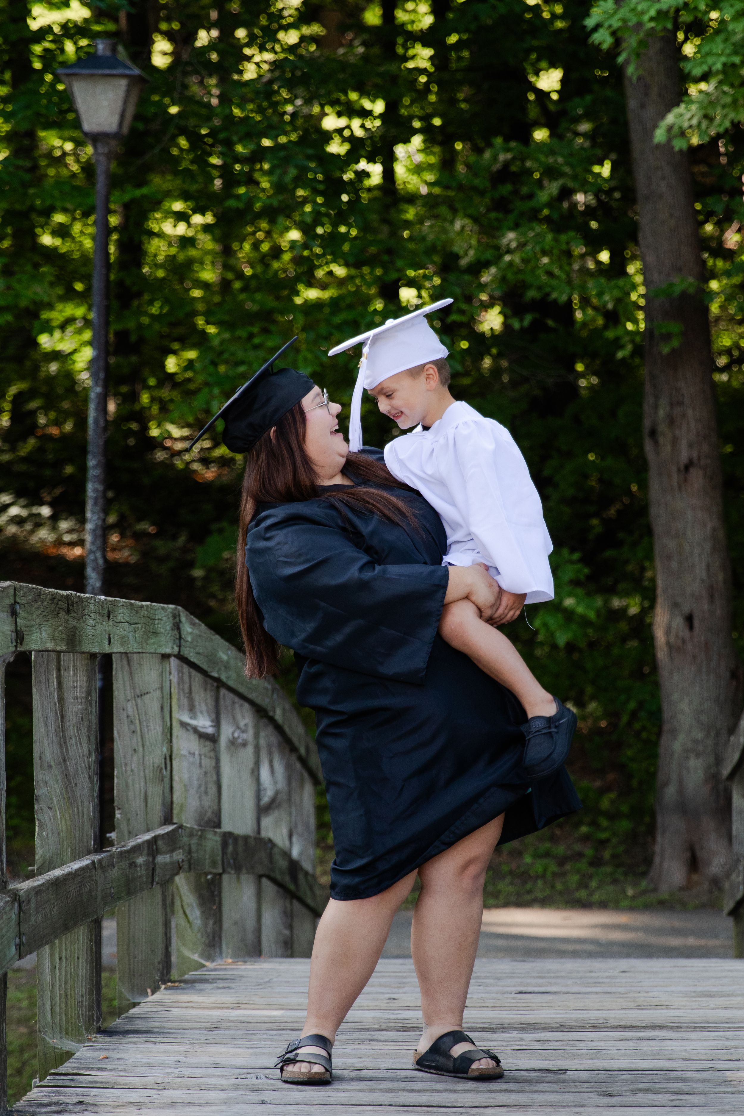 A senior older sister holding her younger brother wearing their cap and gowns. They are smiling joyfully.