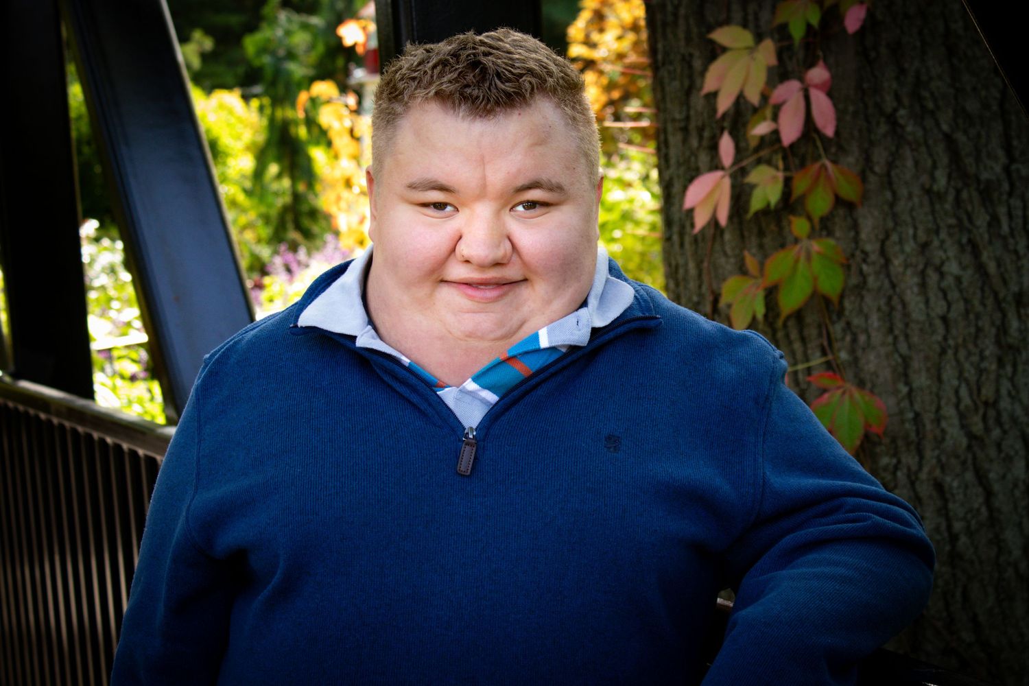 Senior posing for portraits with a relaxed and confident smile on a bridge surrounded by trees and fall colors.