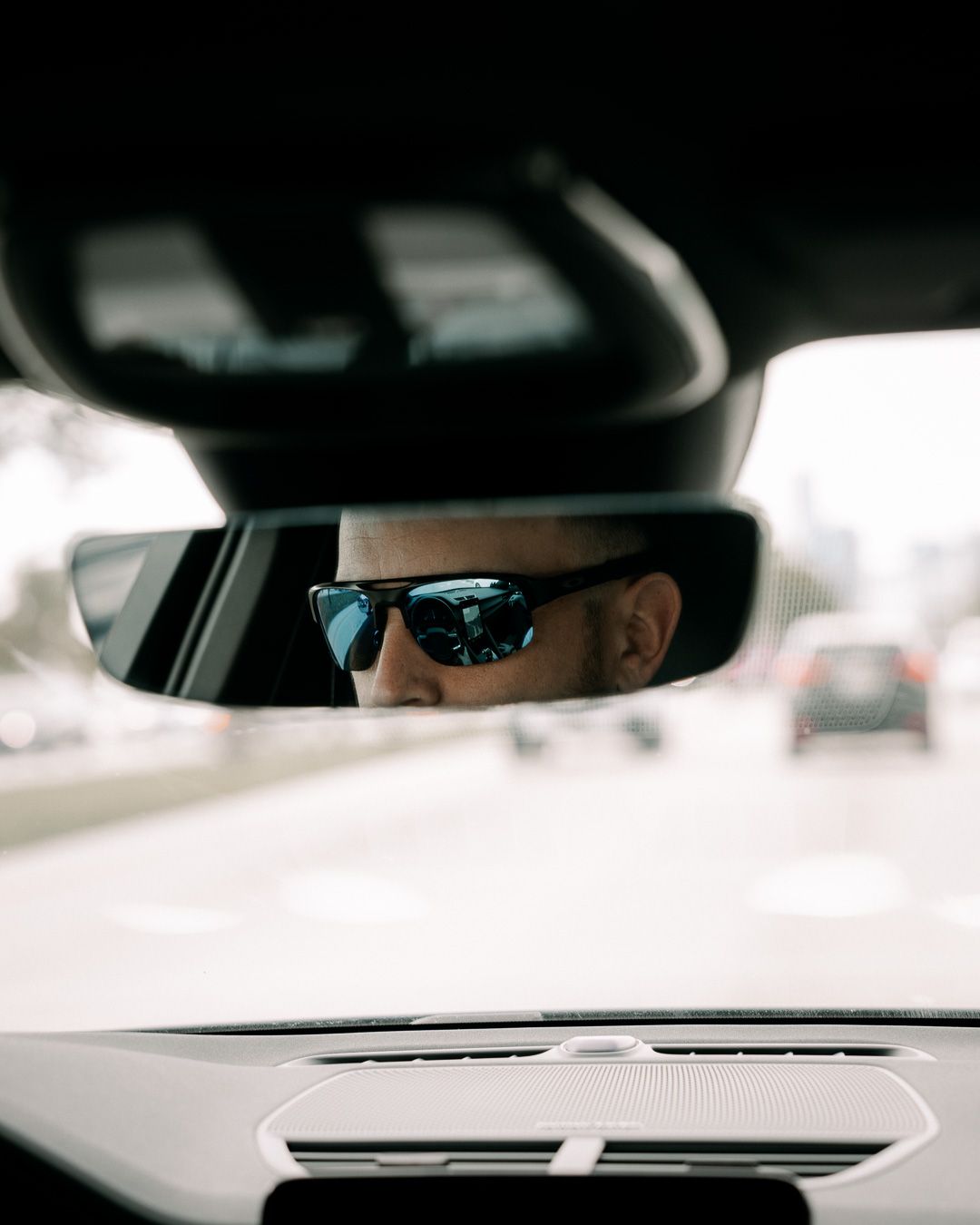 Rearview mirror reflection showing sunglasses while driving.