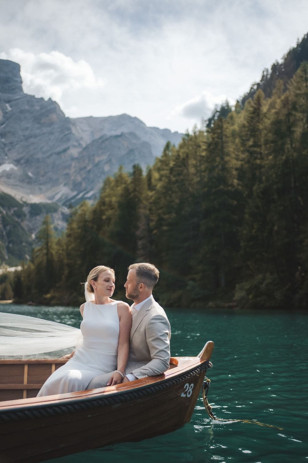 Adventurous elopement photographer capturing a romantic couple on a wooden boat at Lago di Braies, Dolomites.