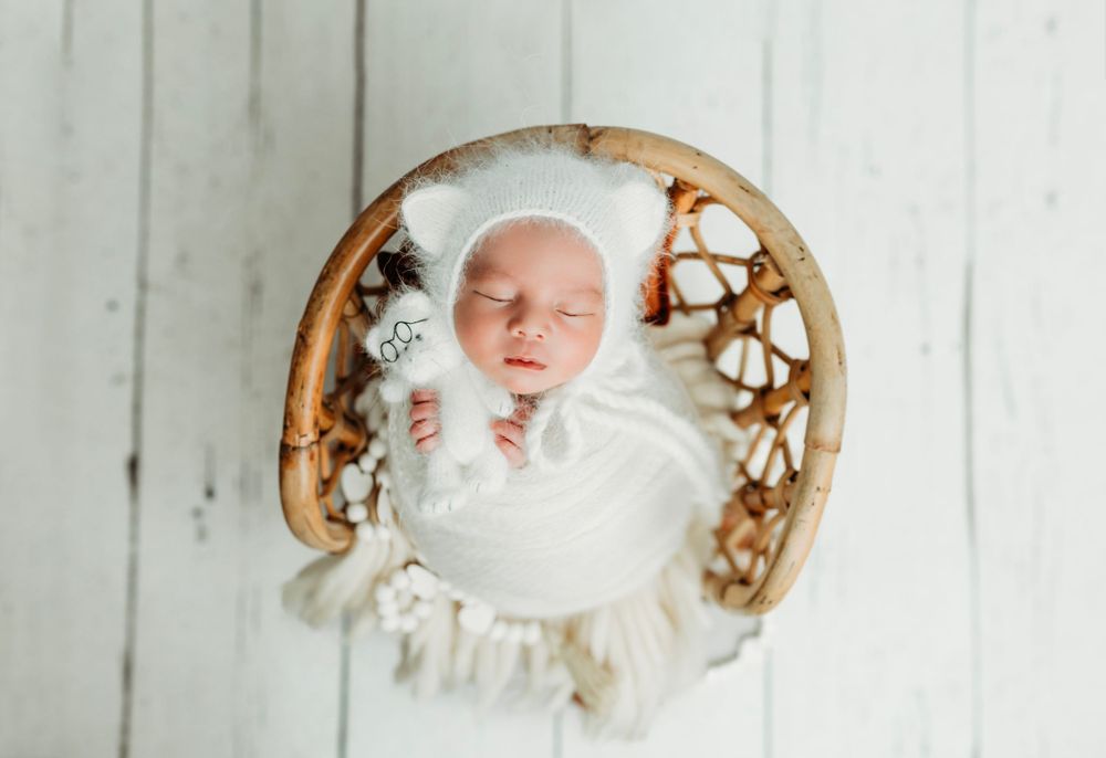 Artistic newborn photography setup with white wrapping and rustic wooden bowl on white planks.