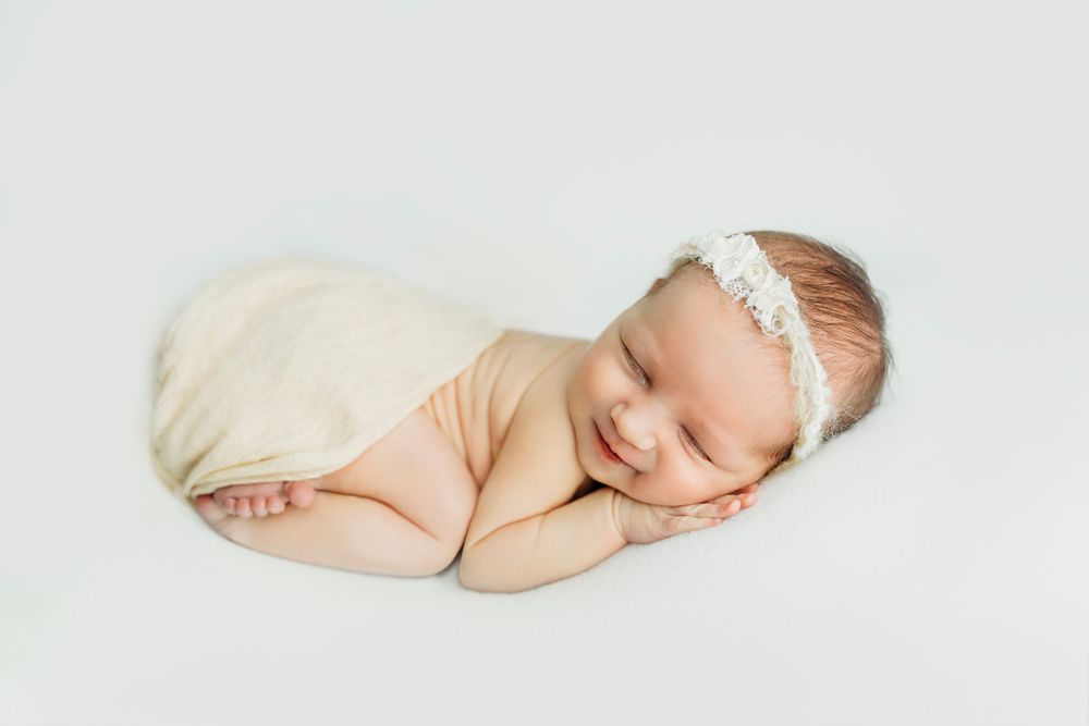 Minimalist newborn portrait series on cream background with delicate headband accent.