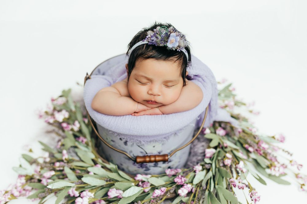 Professional newborn portrait series with spring flowers and soft purple styling.