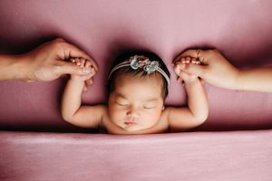 Creative newborn photography series with baby in soft pink lighting and artistic poses.