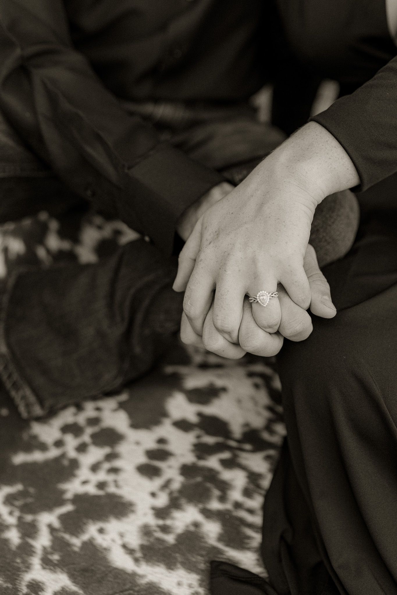 Intimate black and white photo of hands with rings on patterned fabric.