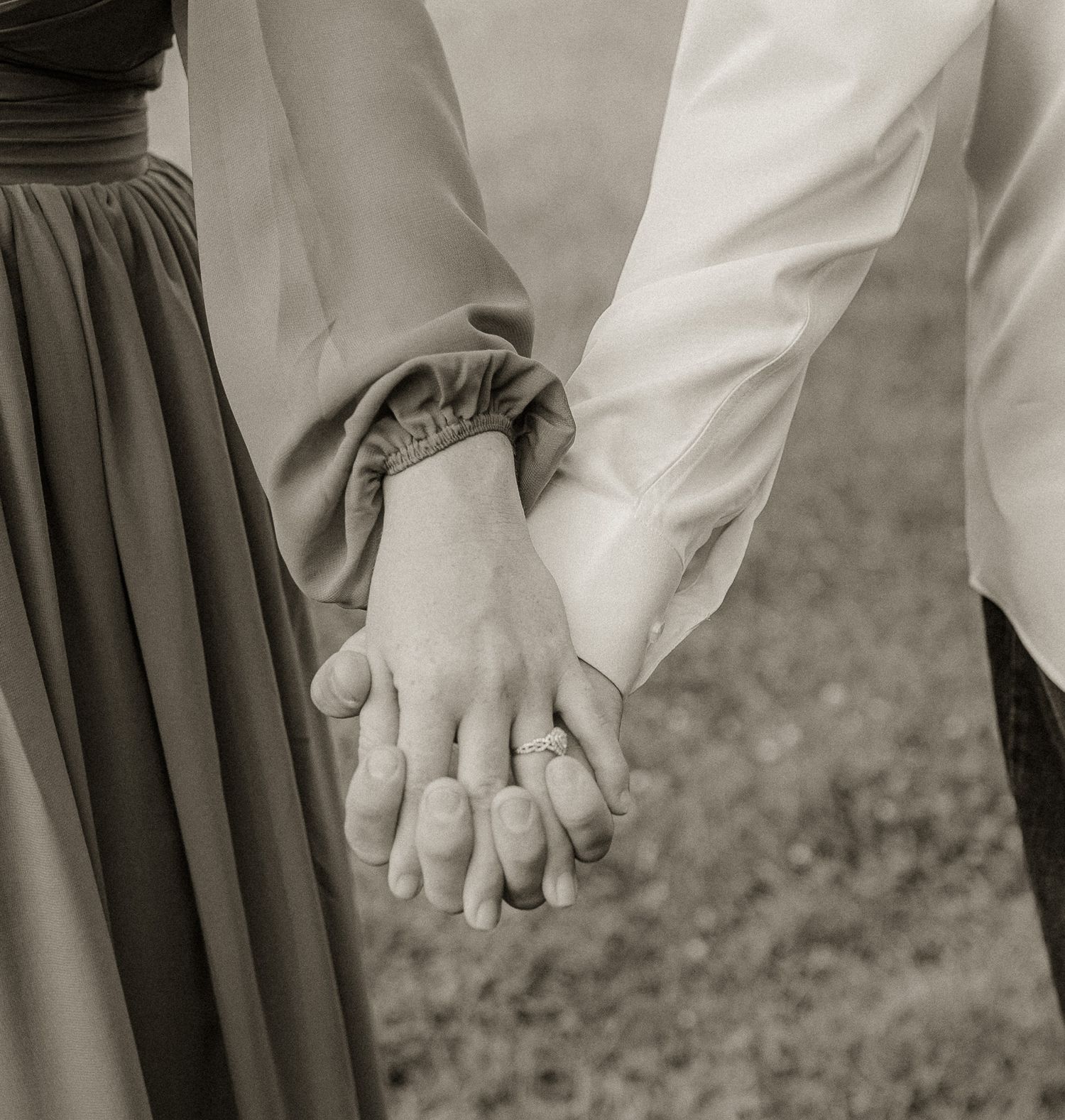 Black and white photograph capturing joined hands in formal wedding attire.