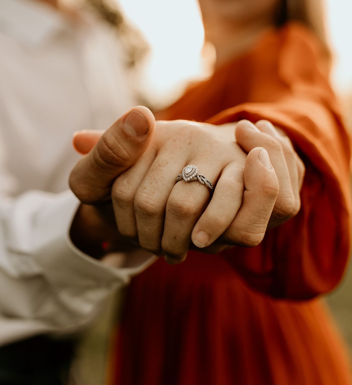 Two hands intertwined showing off an engagement ring against a red dress backdrop.