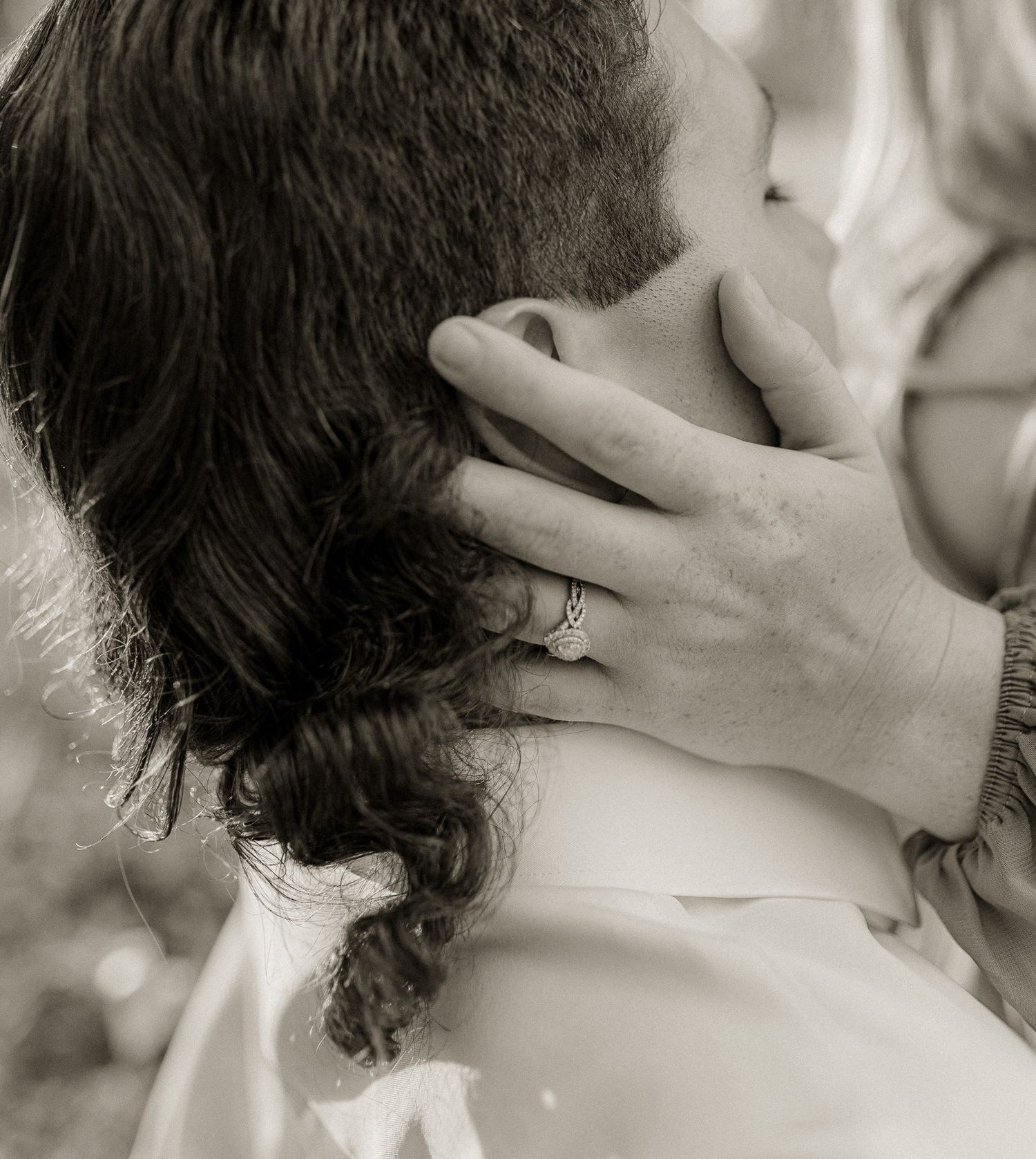 A tender black and white photograph showing hands caressing with a ring visible.