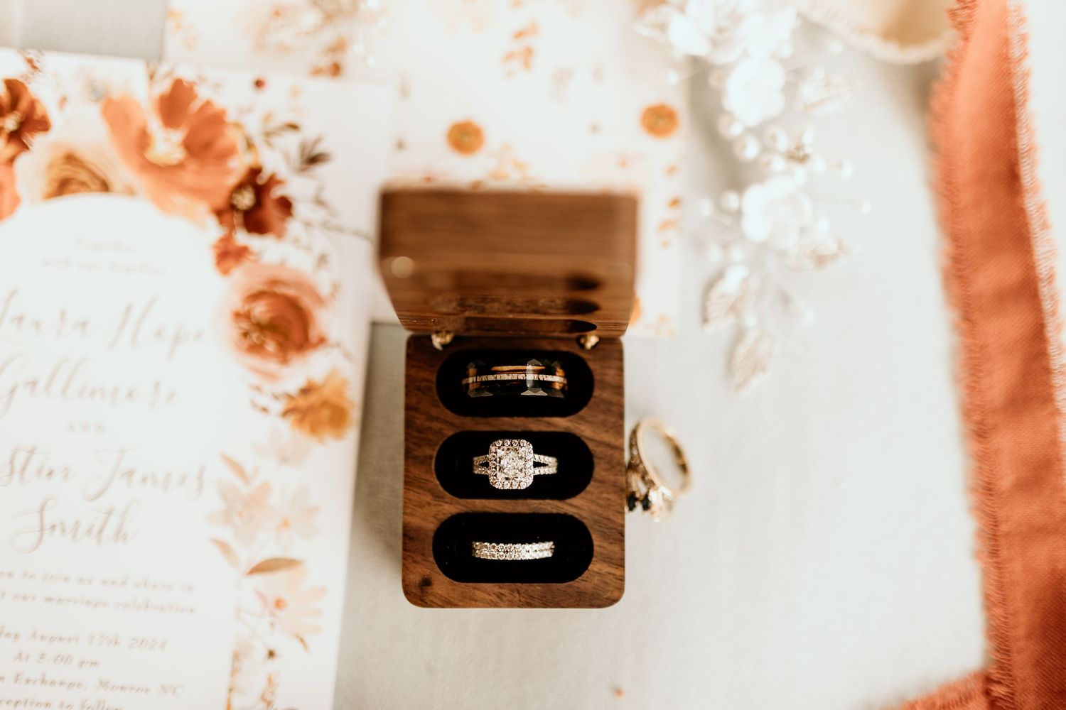 Wedding details and rings photographed on peach-tinted stationery and wooden surfaces.