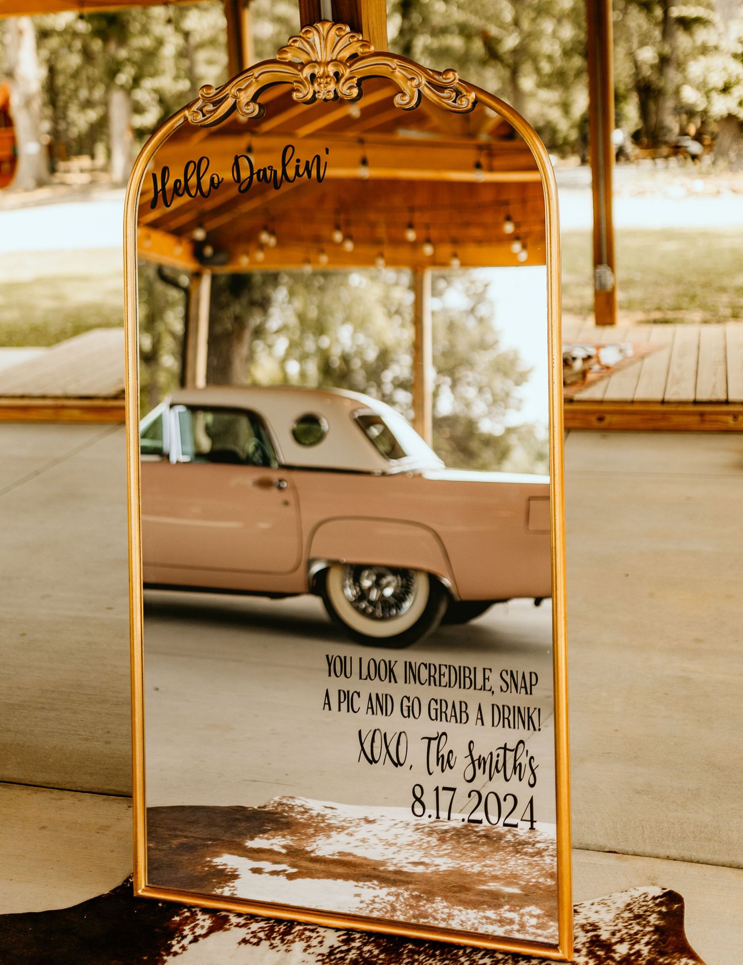 Decorative golden mirror frame displaying wedding date text in outdoor setting.