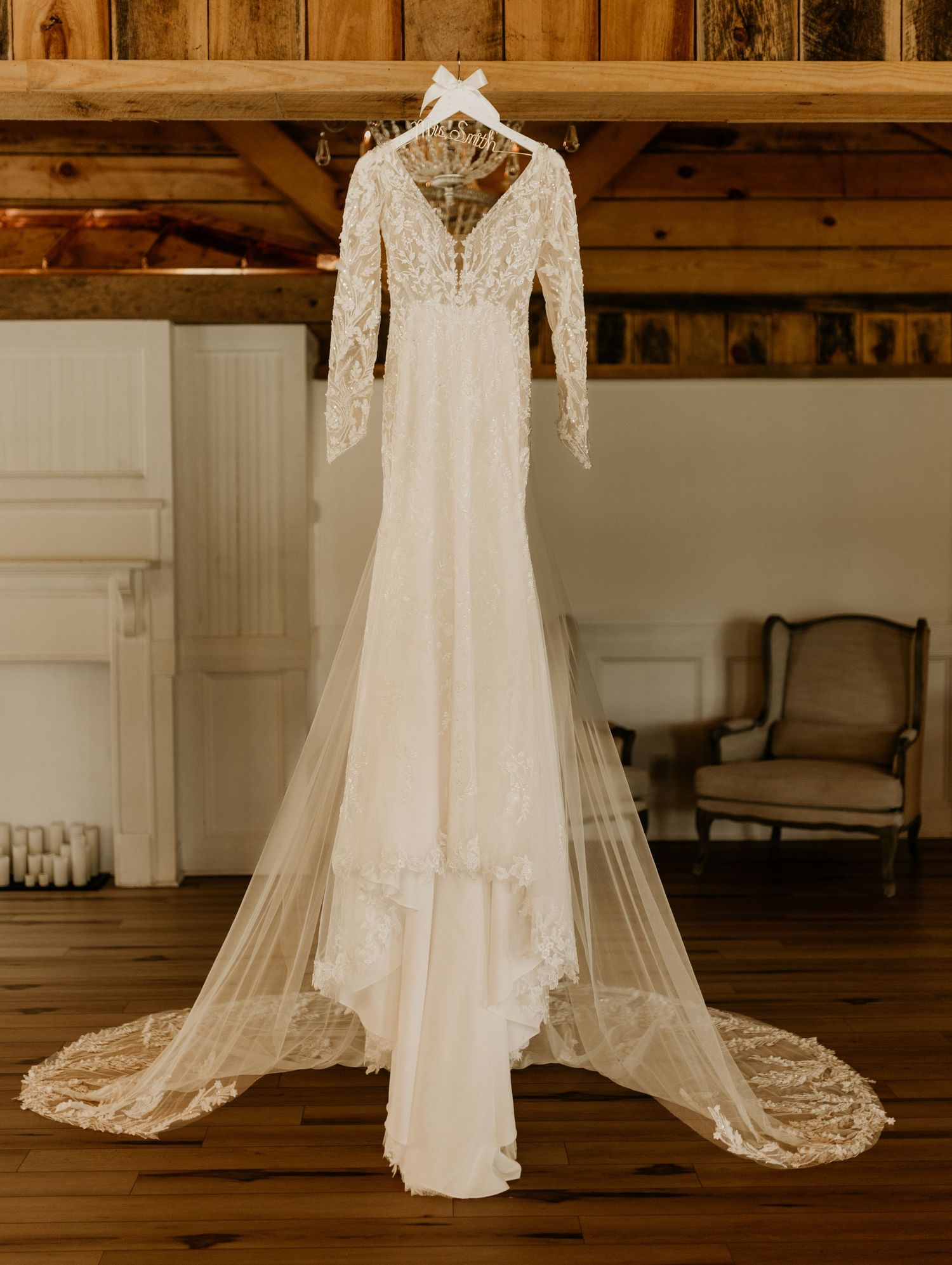 Elegant lace wedding dress displayed hanging against rustic wooden barn interior.
