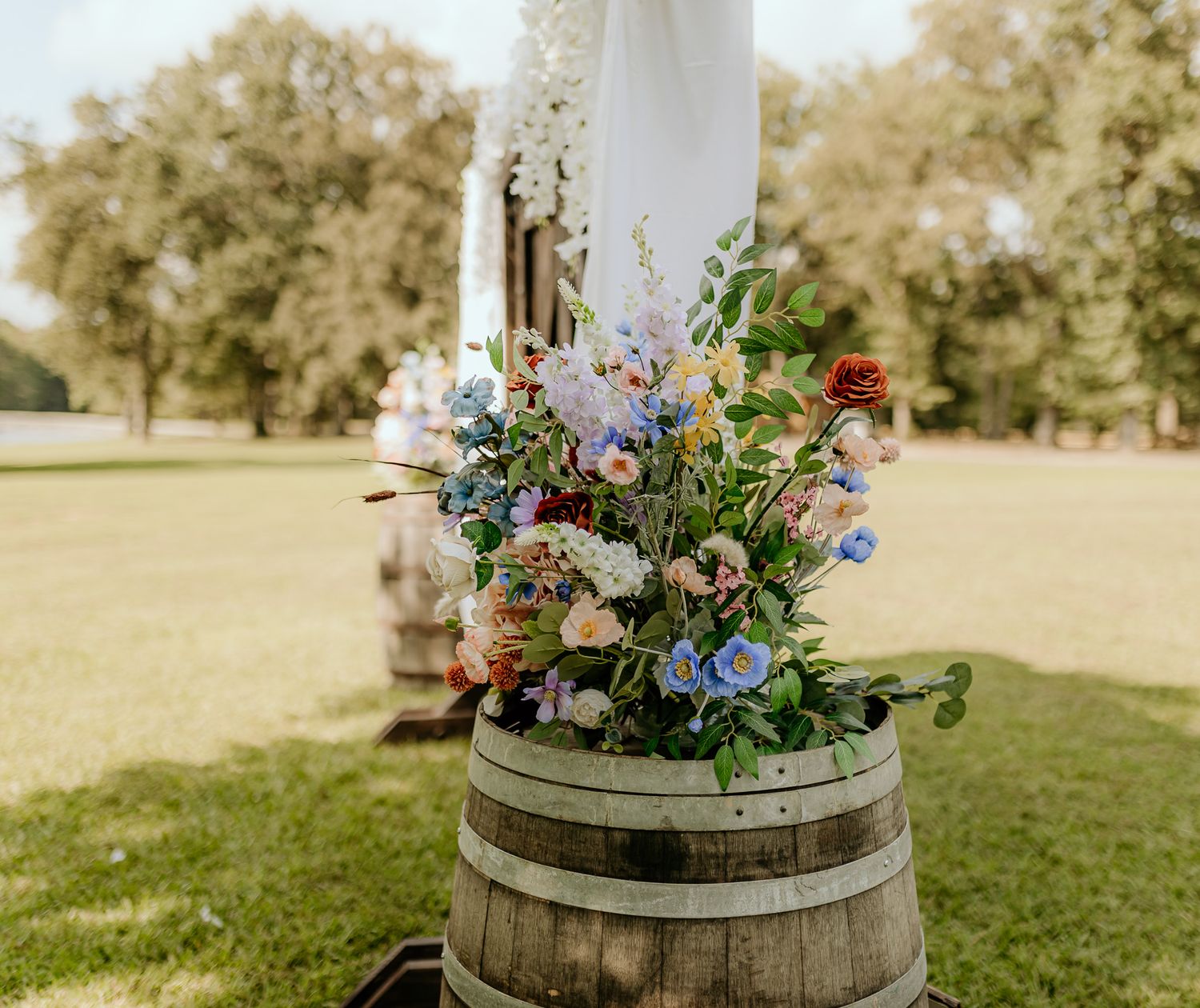 Rustic outdoor wedding decor with floral arrangements on wooden barrels.