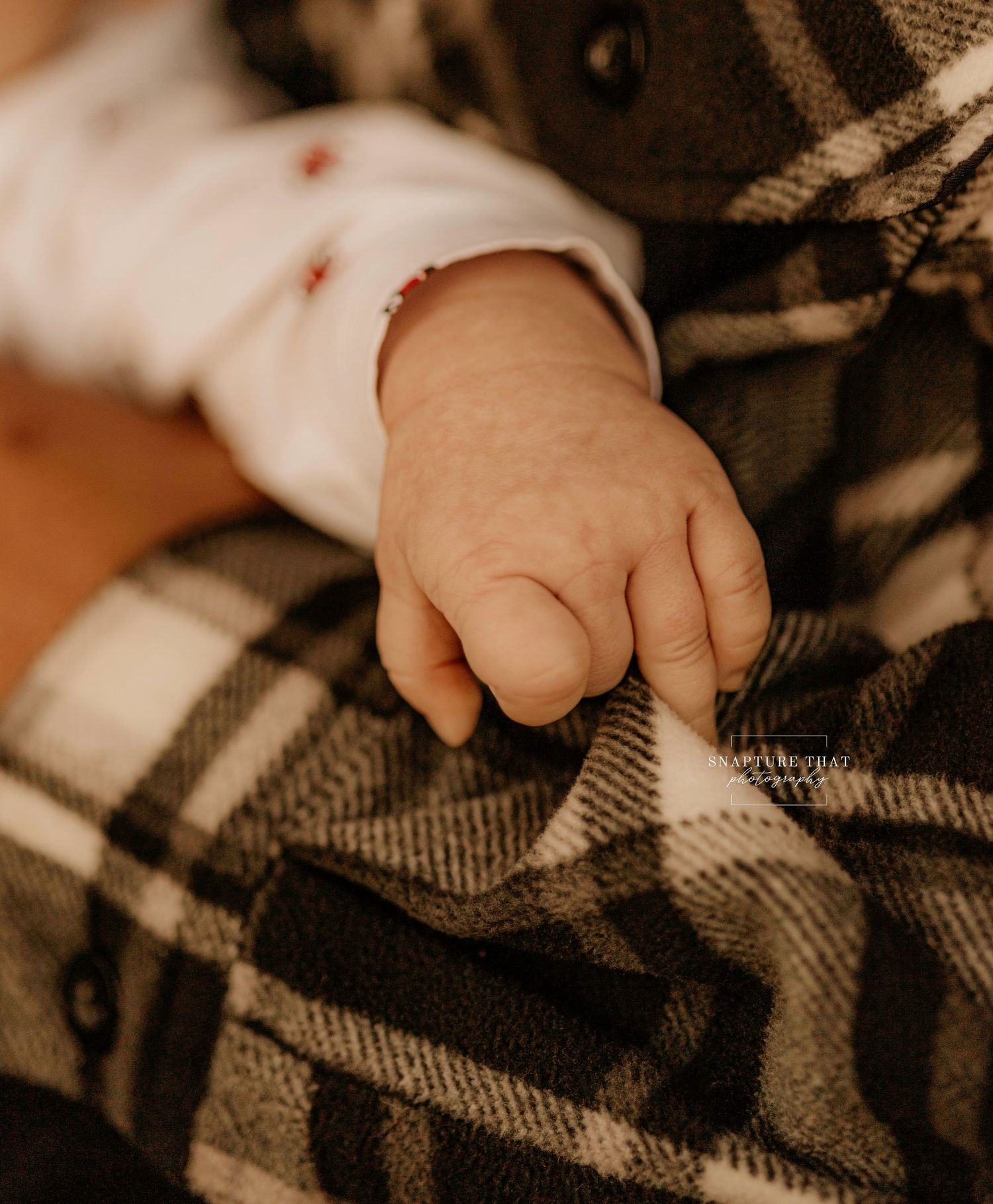 Close-up of baby's hand against plaid blanket in warm sepia tones.