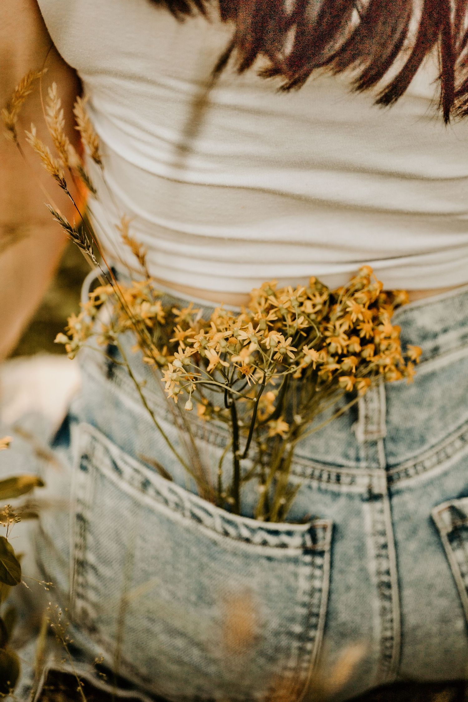 Yellow wildflowers tucked into light wash denim jeans pocket with white top.