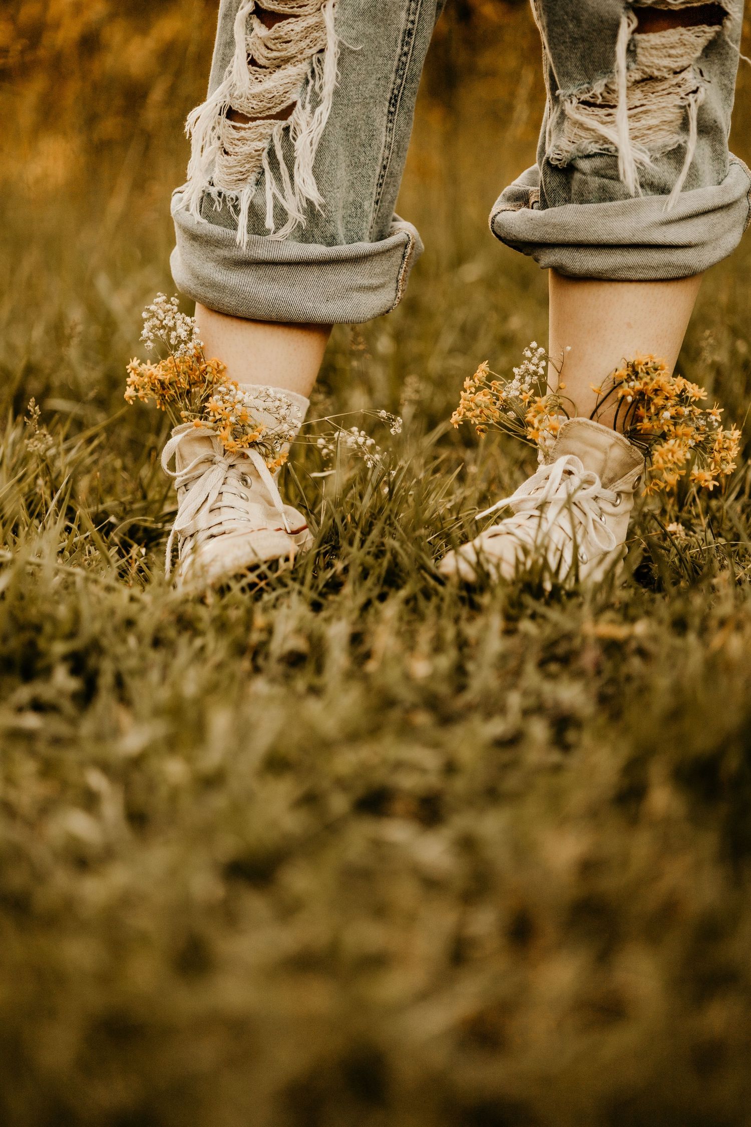 Worn white sneakers standing among wild yellow flowers in golden light.