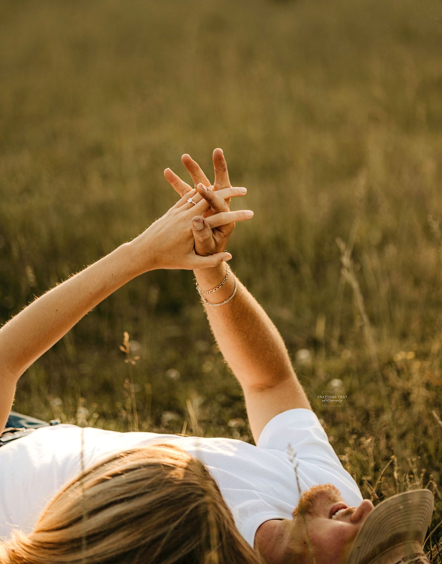 Hands reaching up towards sky while lying in golden grass field.