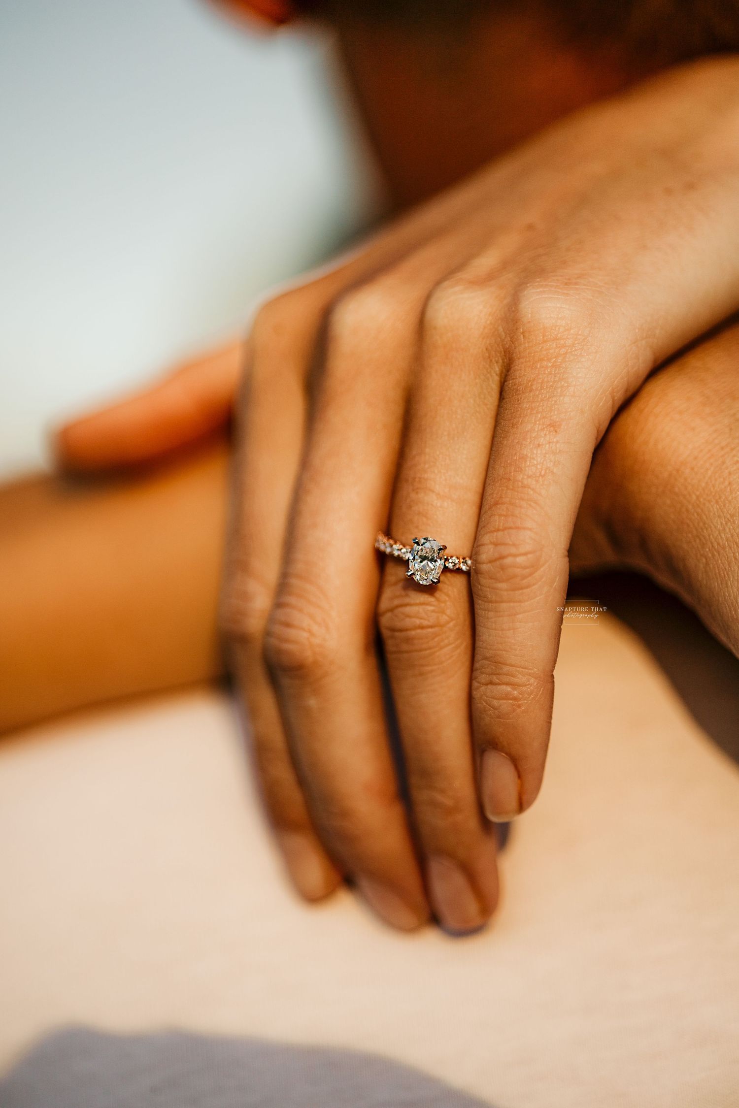 Close-up of hands with an elegant engagement ring against a soft background.