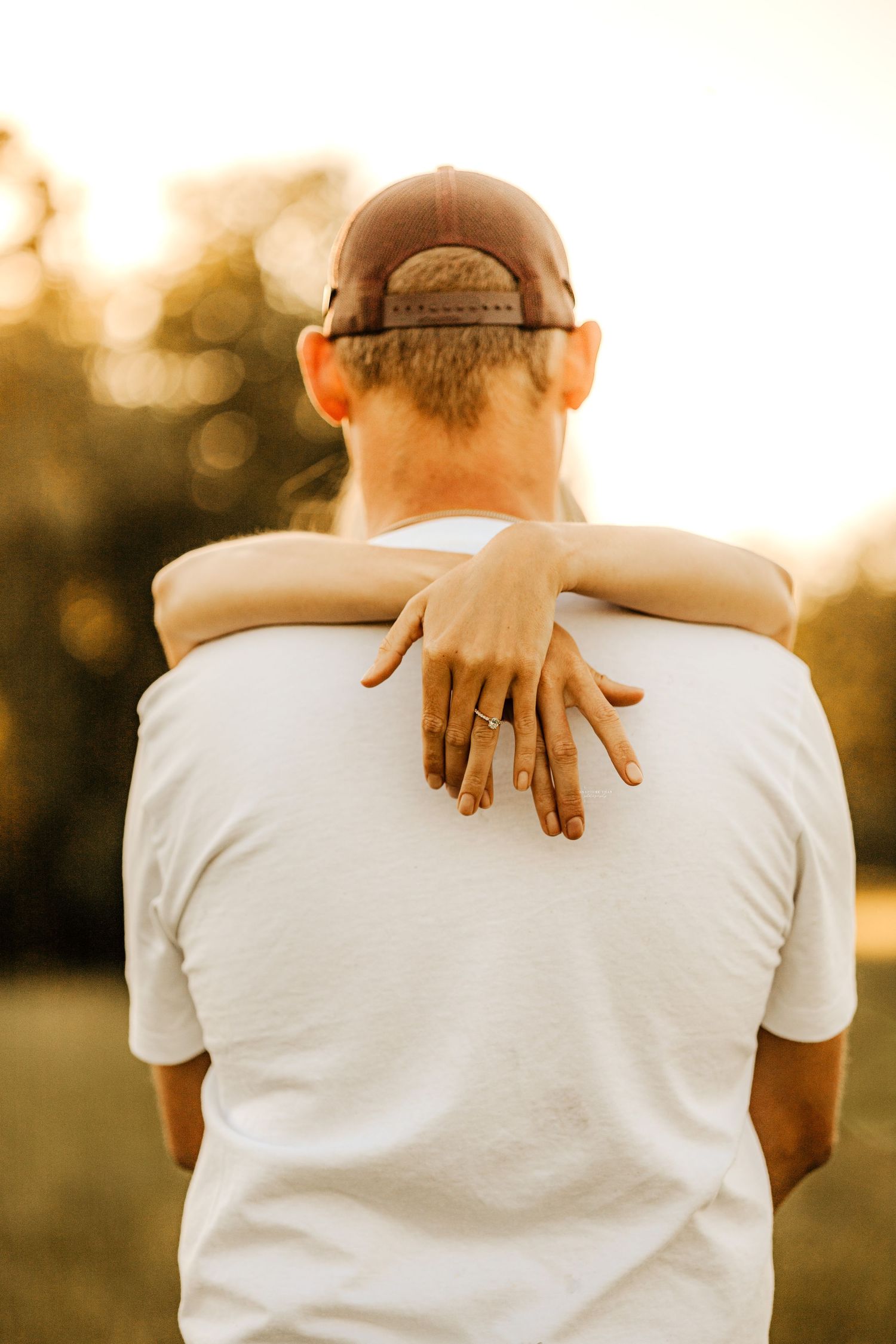 Back view of person wearing white shirt with hands resting on shoulders during golden hour.