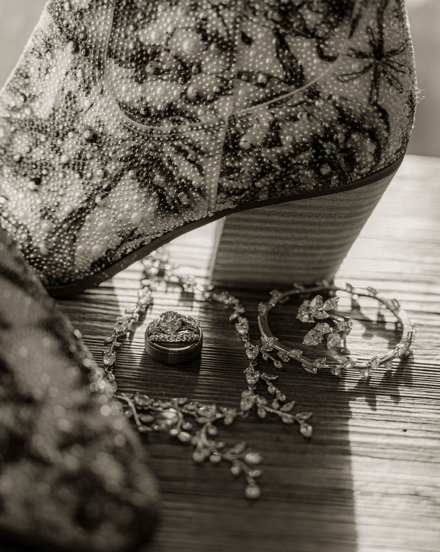 Wedding rings and jewelry displayed beneath patterned boot heel in black and white photography.