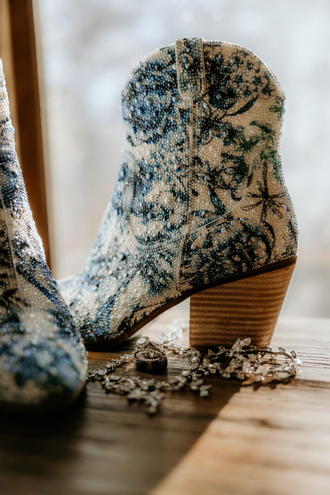 Detailed shot of blue floral patterned cowboy boot with wedding rings on wooden surface.