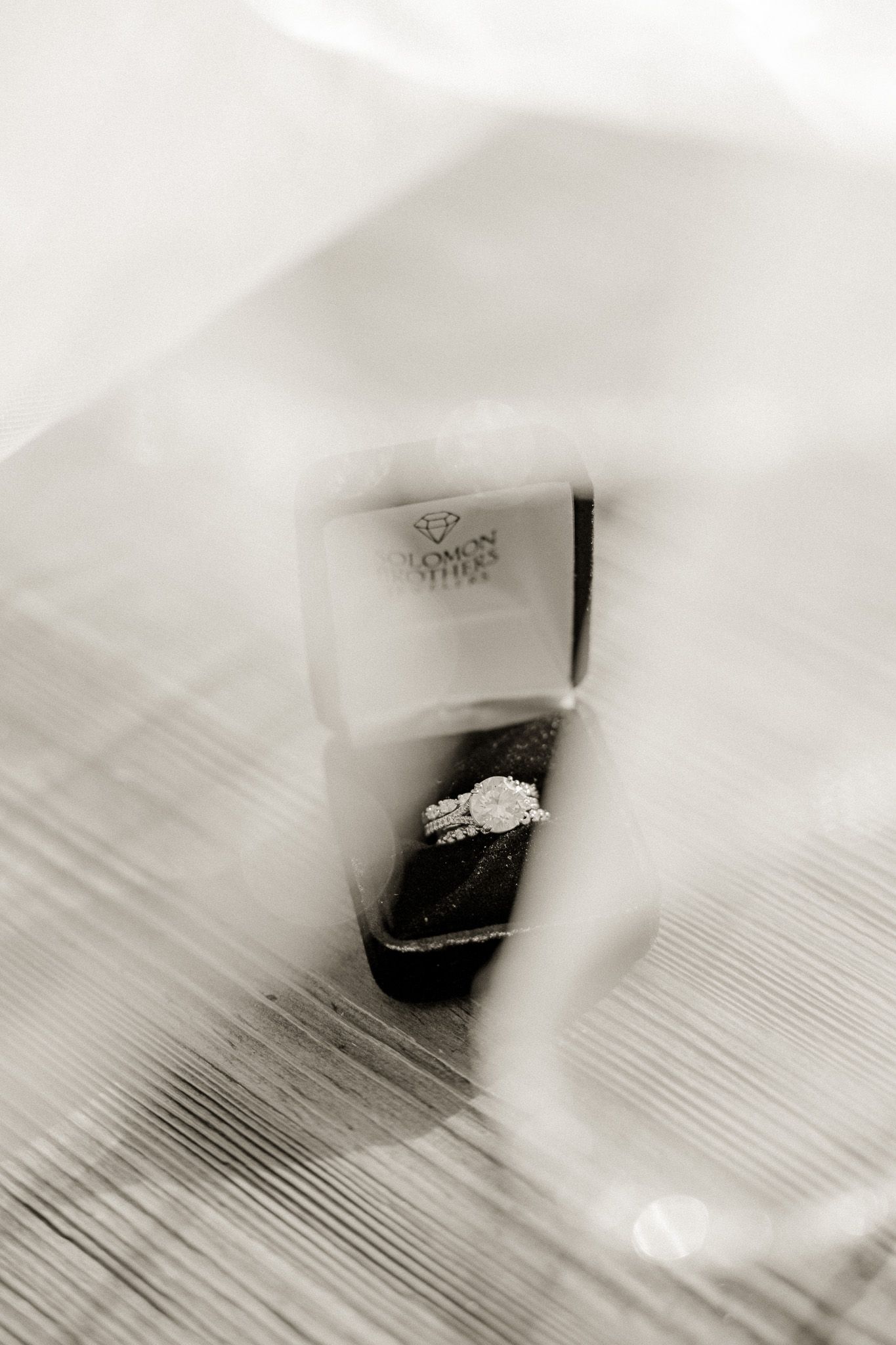 Diamond ring in black box viewed through delicate white veil creating dreamy effect.