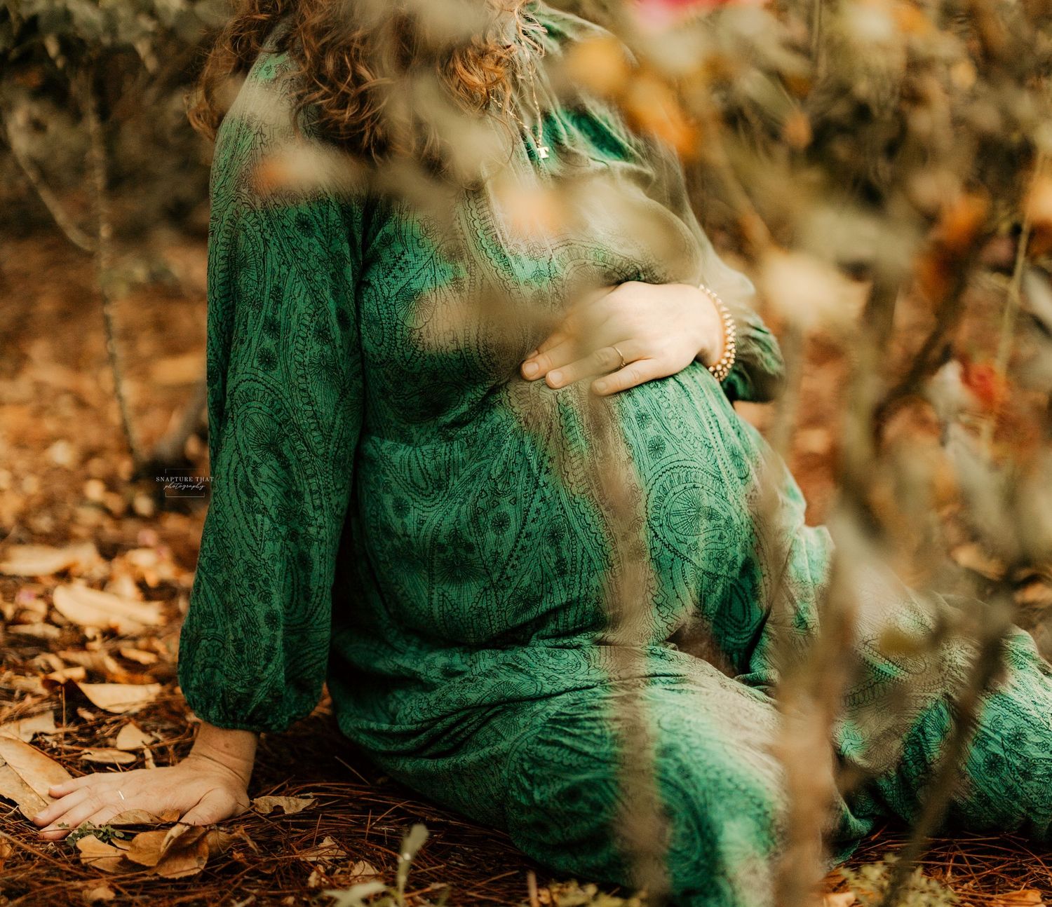 Woman in emerald green lace dress poses gracefully among autumn leaves in a dreamy outdoor setting.