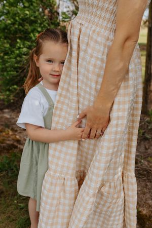 Child in green dress holding parent's hand against gingham dress in garden. Family session in Lake Geneva, Wisconsin.