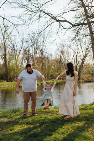 Family playing together by river with bare trees in background. Family session in Lake Geneva, Wisconsin.
