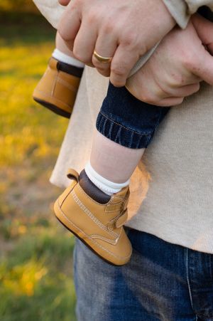 Close-up of baby shoe and wedding rings held in hands against yellow flower background. Family session in Lake Geneva, Wisconsin.