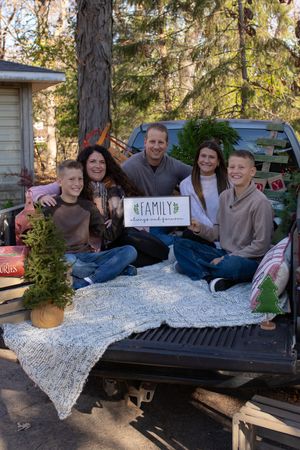 People sitting on the back of a pickup truck with a blanket and family sign in an outdoor setting.