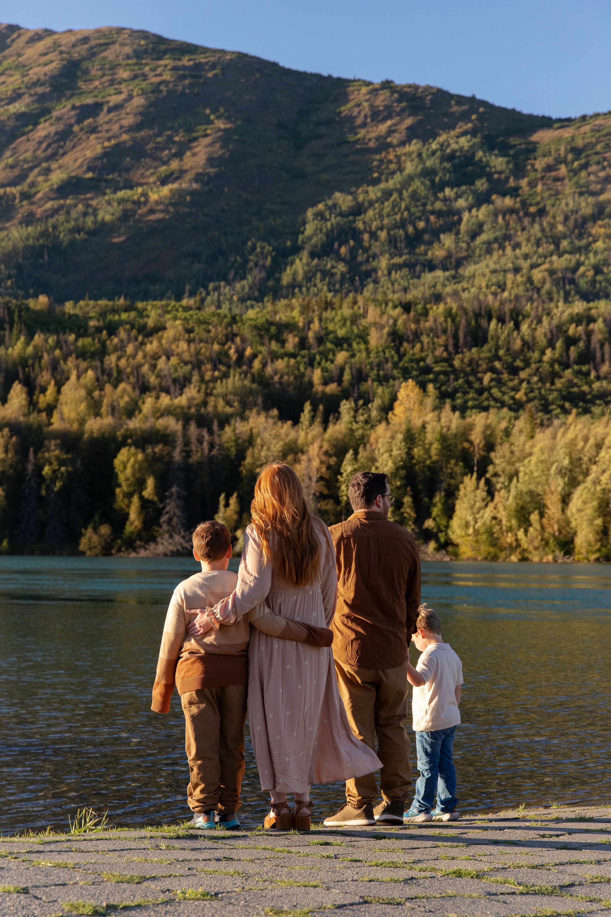 Family sitting together by a scenic mountain lake during golden hour in Cooper Landing, Alaska.